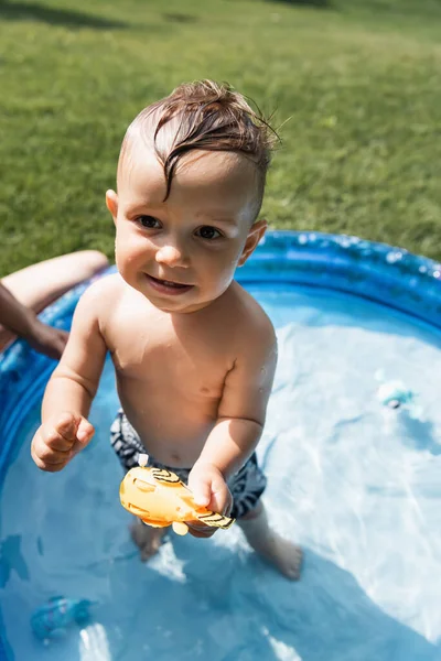 Hochwinkelaufnahme eines lächelnden Kleinkindes, das mit Gummispielzeug in einem aufblasbaren Pool steht — Stockfoto