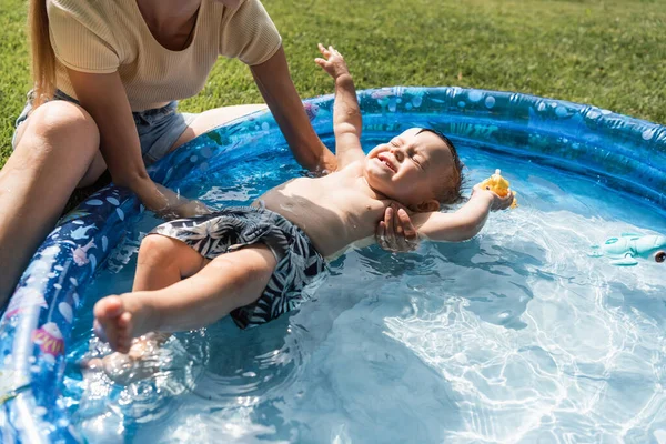 Mother supporting toddler son with closed eyes swimming in inflatable pool — Stock Photo