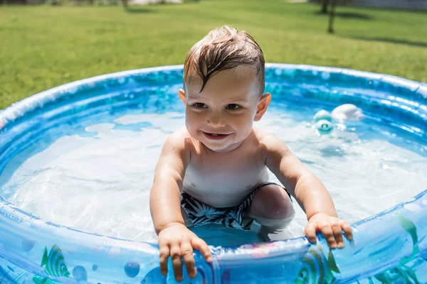 Niño sonriente sentado en la piscina inflable - foto de stock