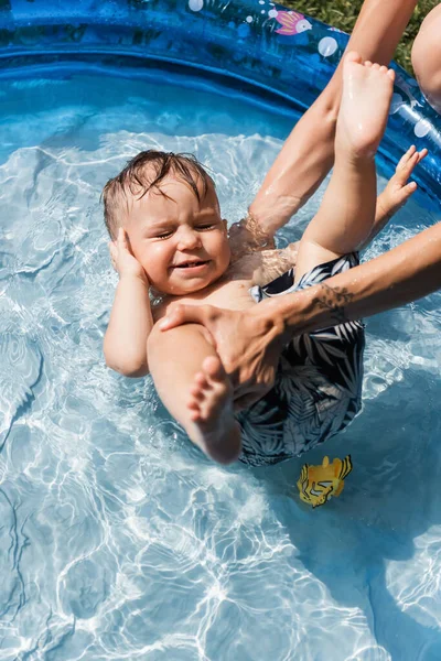Madre tatuada bañando a su hijo pequeño en piscina inflable - foto de stock