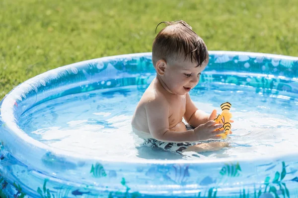 Toddler boy playing with rubber toy in blue inflatable pool — Stock Photo