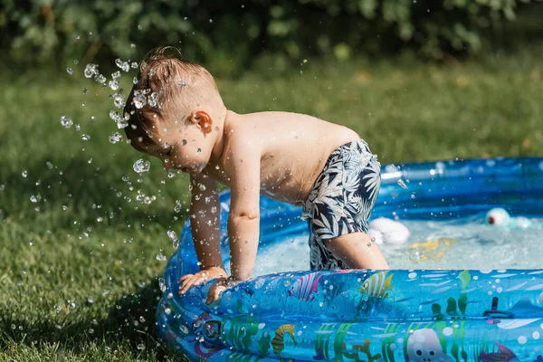 Salpicaduras cerca del niño pequeño en la piscina inflable - foto de stock