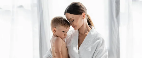 Caring mother in bathrobe holding in arms naked toddler son, banner — Stock Photo