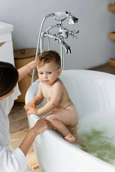 Mutter schaut Kleinkind in Badewanne an — Stockfoto