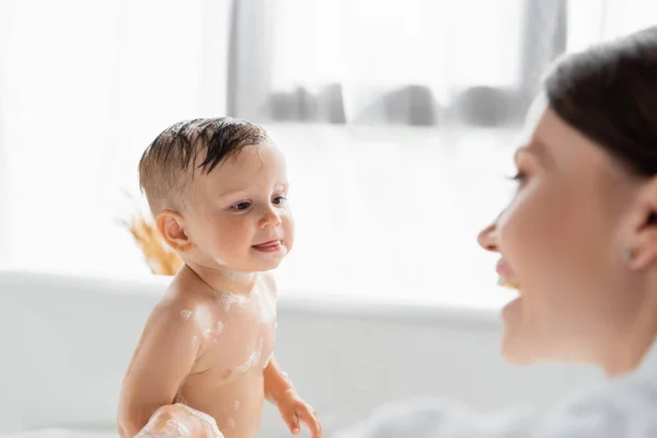 Wet toddler boy sticking out tongue near blurred and cheerful mother on foreground — Stock Photo