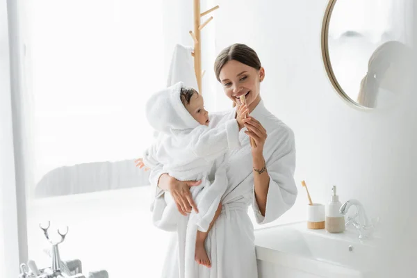 Glückliche Mutter hält Kleinkind-Sohn im Bademantel und Zahnbürste im Arm — Stockfoto