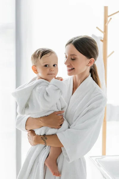 Happy mother looking at toddler son in bathrobe — Stock Photo