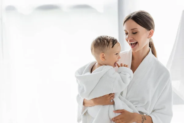 Erstaunte Mutter schaut Kleinkind im Bademantel an — Stockfoto