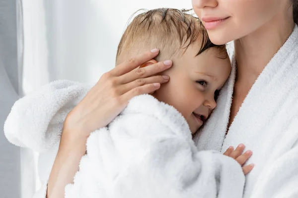 Young mother holding in arms happy toddler son in bathrobe — Stock Photo