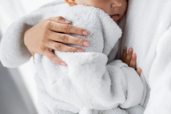 Ausgeschnittene Ansicht einer jungen Mutter, die Kleinkind-Sohn im Bademantel in den Armen hält — Stockfoto