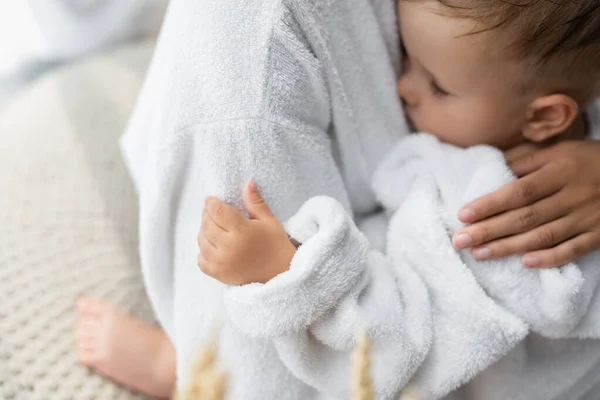 Madre abrazando hijo pequeño con los ojos cerrados en albornoz - foto de stock