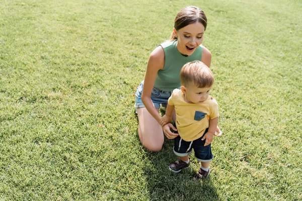 Amazed mother looking at toddler son standing on green grass — Stock Photo