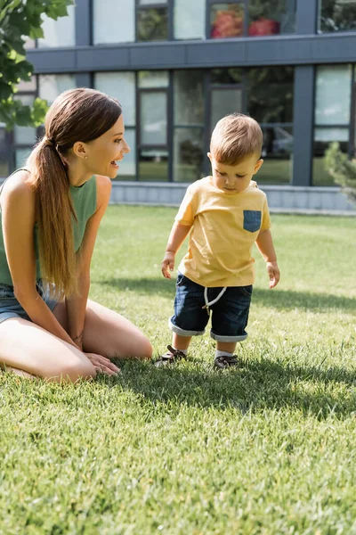 Mère excitée regardant tout-petit fils debout sur l'herbe verte — Photo de stock