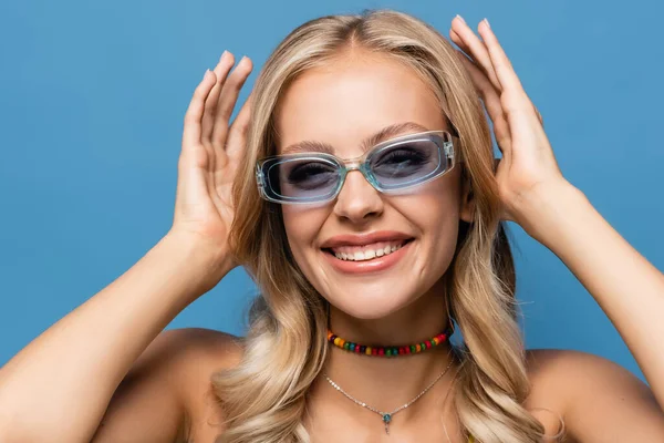 Весела молода жінка в модних сонцезахисних окулярах посміхається ізольовано на синьому — стокове фото