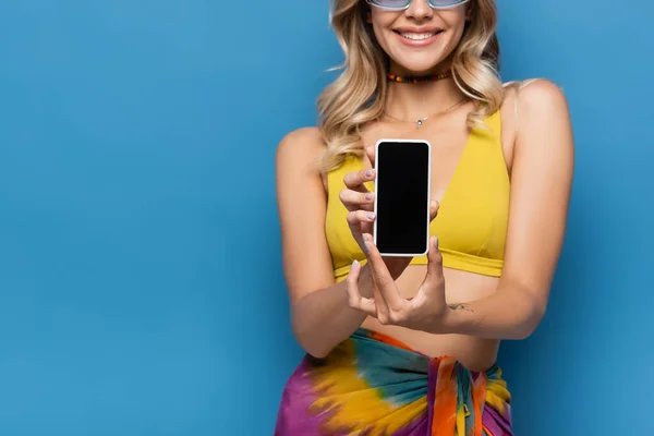 Vista recortada de la joven feliz en bikini amarillo superior celebración de teléfono inteligente con pantalla en blanco aislado en azul - foto de stock