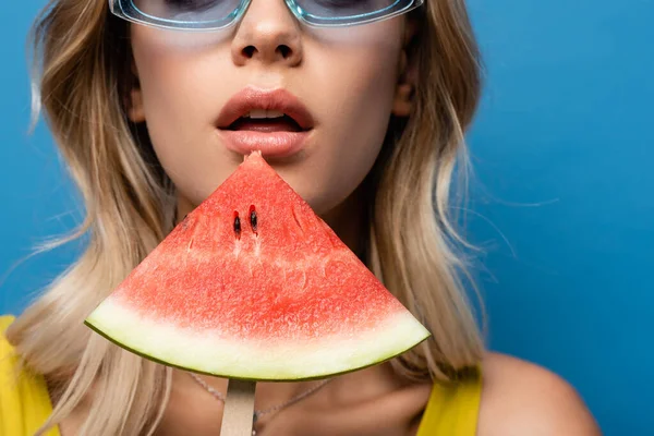 Vista recortada de la joven mujer sosteniendo palillo de paleta con sandía aislada en azul - foto de stock