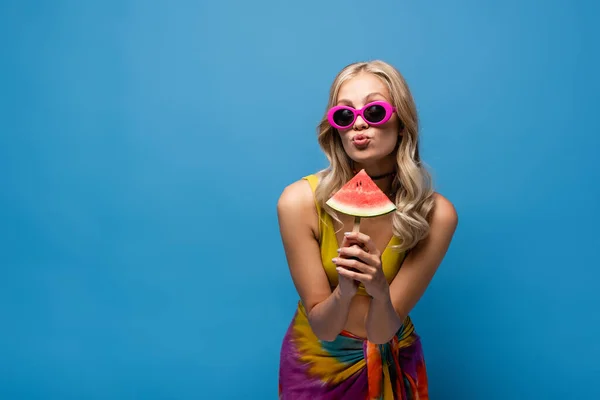 Young woman pouting lips and holding popsicle stick with fresh watermelon isolated on blue — Stock Photo
