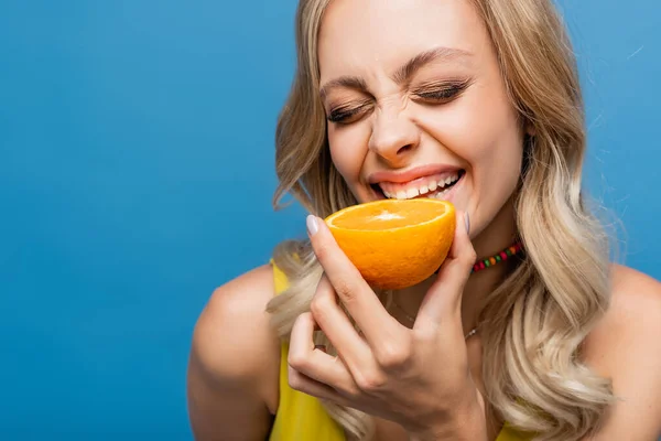 Щаслива молода жінка в жовтому бікіні зверху кусає апельсин ізольовано на синьому — стокове фото
