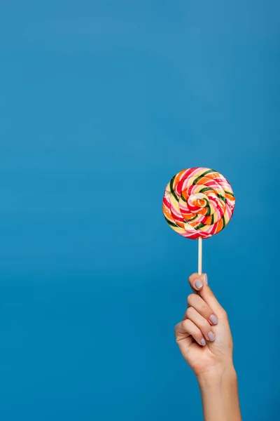 Cropped view of woman holding sweet lollipop isolated on blue — Stock Photo