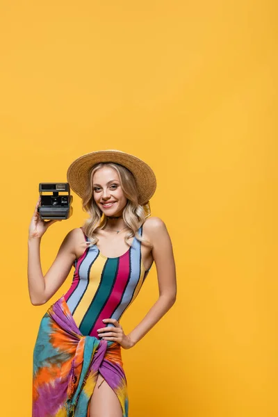 Joyful woman in straw hat posing with vintage camera isolated on yellow — Stock Photo