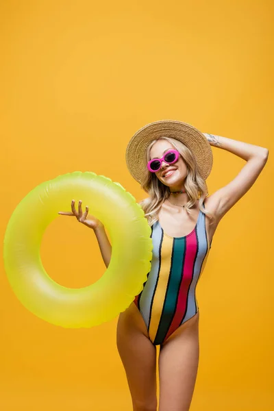 Smiling woman in straw hat and swimsuit standing with inflatable ring isolated on yellow — Stock Photo