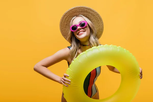 Mulher sorridente em chapéu de sol e maiô segurando anel inflável isolado no amarelo — Fotografia de Stock