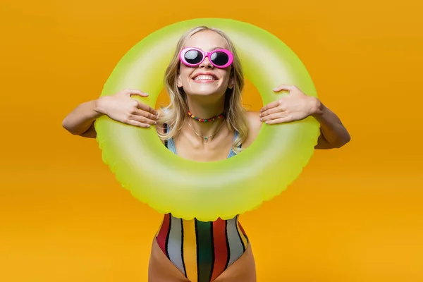 Mujer complacida en gafas de sol y traje de baño sosteniendo anillo inflable aislado en amarillo - foto de stock