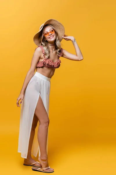 Full length of smiling woman with tattoo standing in ruffle bikini top and white skirt on yellow — Stock Photo