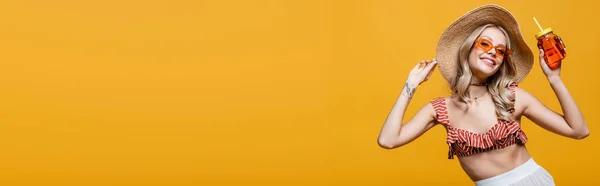 Smiling woman in straw hat and sunglasses holding alcohol cocktail isolated on yellow, banner — Stock Photo