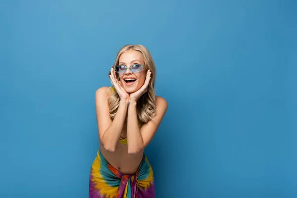 Excitée jeune femme en lunettes de soleil regardant loin isolé sur bleu — Photo de stock