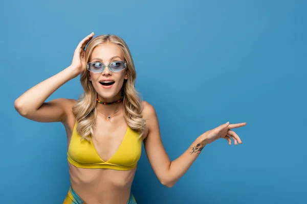Amazed young woman in bikini top pointing away isolated on blue — Stock Photo