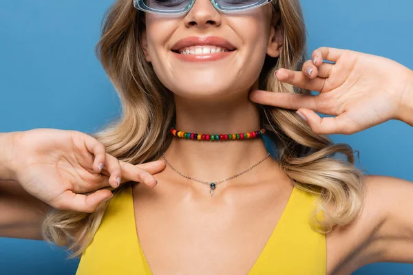 Corte vista de alegre jovem mulher em frisado colar colorido sorrindo isolado no azul — Fotografia de Stock