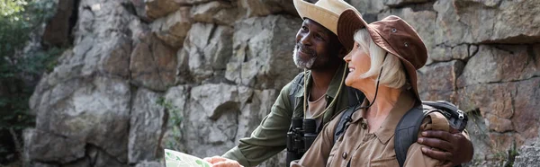 Senior african american hiker hugging smiling wife with map near rock, banner — Stock Photo