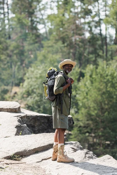 Senior african american hiker holding backpack on rock — Stock Photo