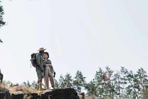 Seniorin lächelt Mann mit Rucksack auf Felsen im Wald an — Stockfoto