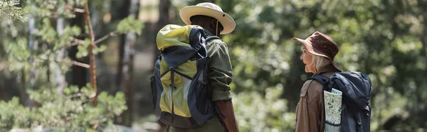 Smiling hiker with backpack looking at african american husband in forest, banner — Stock Photo