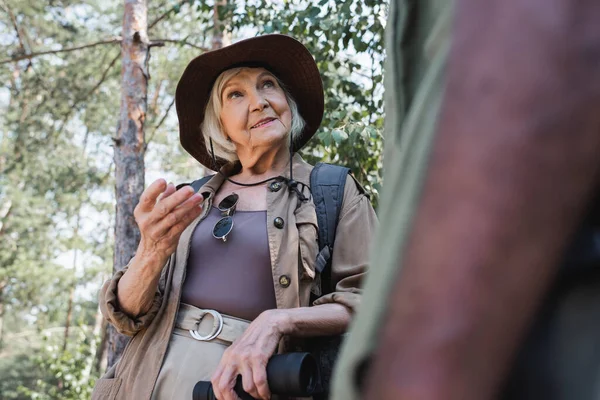 Low angle view of smiling traveler with binoculars looking at african american husband on blurred foreground — Stock Photo