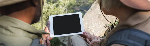 Cropped view of interracial tourists using digital tablet in forest, banner — Stock Photo