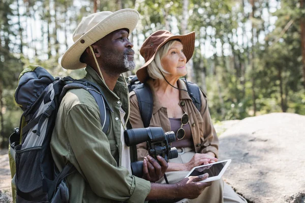 Африканский турист держит цифровой планшет и бинокль рядом с женой на скале — стоковое фото