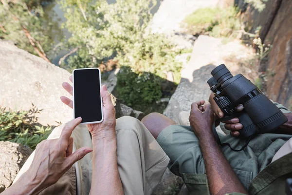 Зверху на смартфон біля африканського чоловіка з біноклем на каміннях. — стокове фото