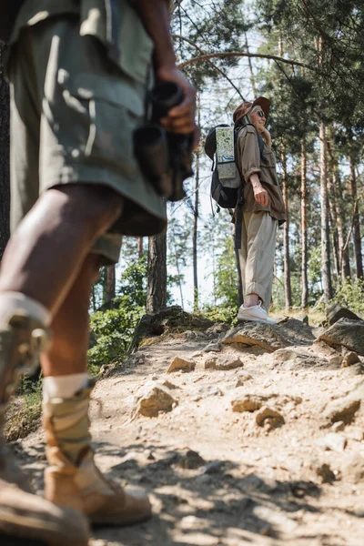 Smiling senior traveler with backpack walking in forest near blurred african american husband — Stock Photo