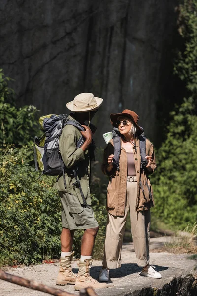 Viajero afroamericano sosteniendo mochila cerca de esposa en bosque - foto de stock