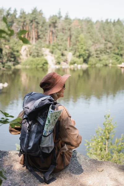 Літні мандрівники з картою і рюкзаком сидять на скелі біля озера — стокове фото