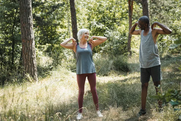 Senior afrikanisch-amerikanischer Mann trainiert neben lächelnder Frau im Wald — Stockfoto