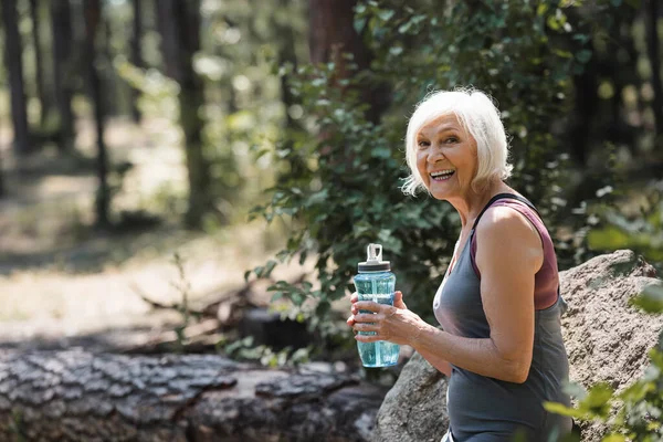 Alegre deportista senior sosteniendo botella deportiva en el bosque - foto de stock