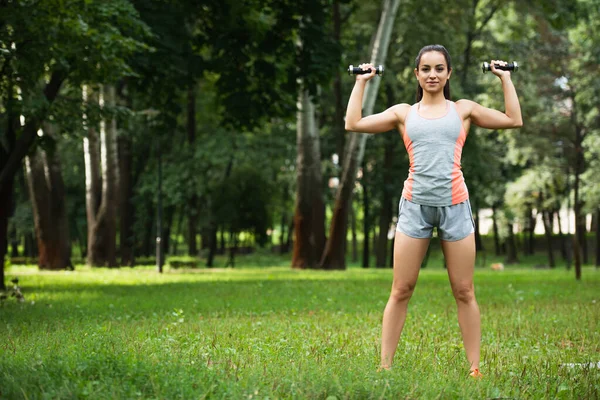 Junge Sportlerin trainiert mit Kurzhanteln im Park — Stockfoto
