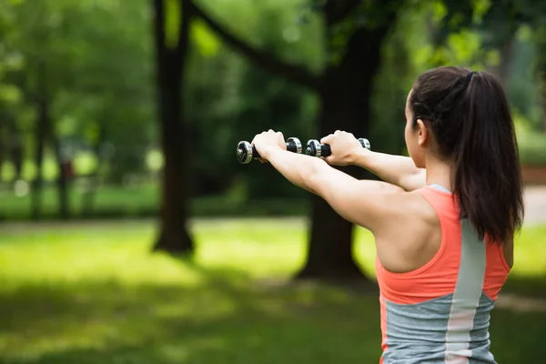 Юная брюнетка спортсменка, занимающаяся спортом с гантелями в парке — стоковое фото
