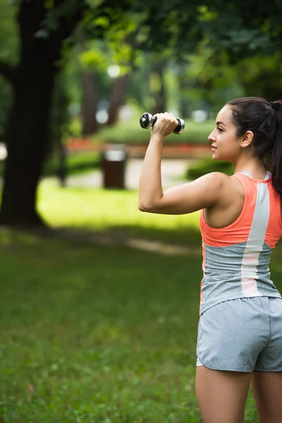 Strong sportswoman exercising with dumbbell in park — Stock Photo