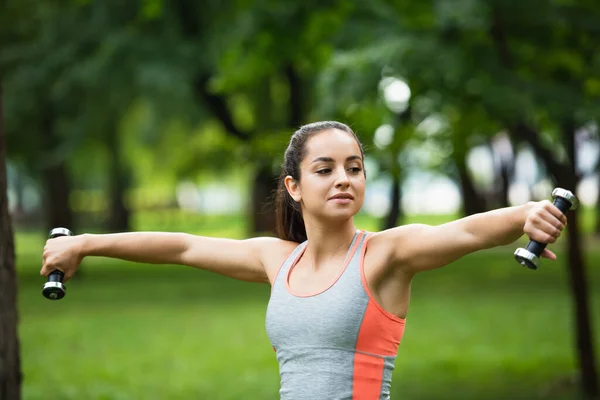 Young sportswoman holding dumbbells in outstretched hands — Stock Photo