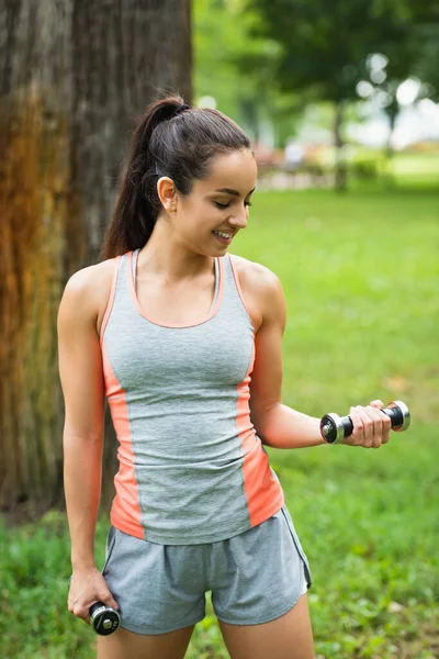 Smiling young sportswoman exercising with dumbbells in park — Stock Photo